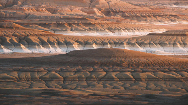 View of layered earth formations displaying textures of brown, white, and gold under the light of setting sun, Kyzylkup, Mangystau Region, Kazakhstan.