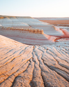 View of the arid landscape with layered rock formations exhibiting warm hues and textured surfaces under a clear sky, Kyzylkup, Mangystau Region, Kazakhstan.