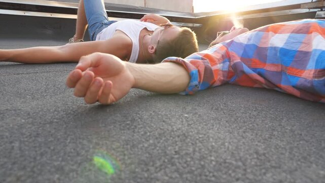 Two young gays lying on roof and smoking with bright sunlight at background. Men resting and enjoying life together. Friends relaxing outdoor at sunset time. Beautiful bottom view Slow mo Close up