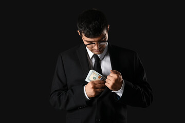 Young businessman putting bribe in jacket on dark background
