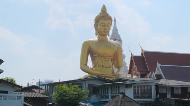 Giant gold Buddha Statue at Wat Paknam Phasi Charoen temple in Bangkok city, Thailand. Big golden buddha statue rising above water canal and temple rooftops. Travel and tourism in Asia