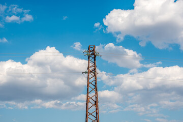 Obraz premium Vintage Rusty Steel Power Pylon under Bright Blue Sky with Cumulus Clouds