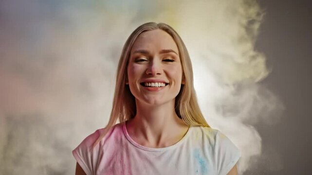 Joyful woman in white t-shirt covered in colorful powder cloud laughing at Holi festival