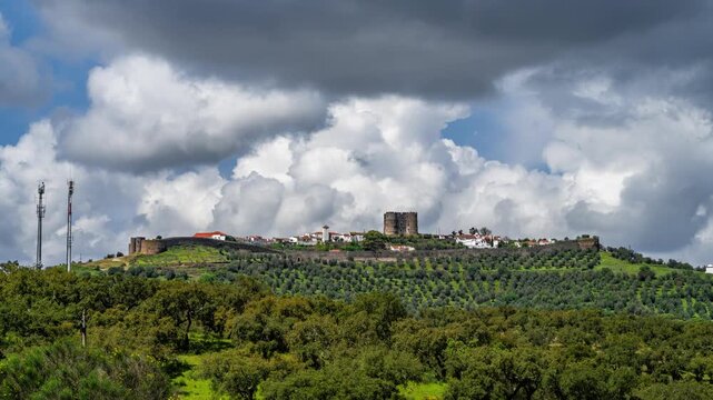 Dramatic timelapse of moving clouds over Evoramonte Castle in Alentejo, Portugal. Sunlight breaking through thick clouds creates dynamic light and shadow over the historic hilltop village.