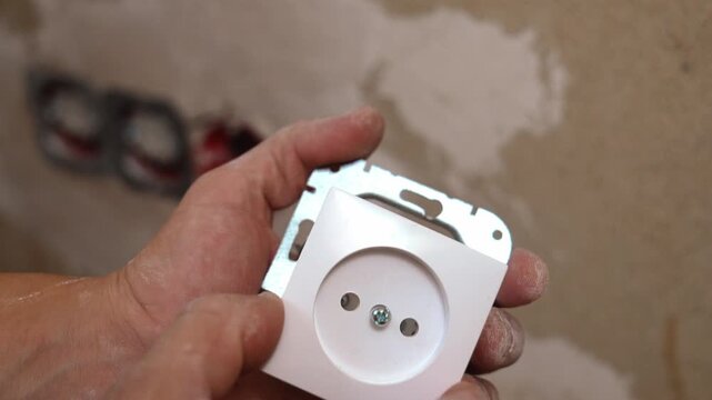 Hand-held wall socket module assembled, showing the front side, metal mounting frame, and internal terminal block. Highlighting the composition with the finished front panel, screw points,