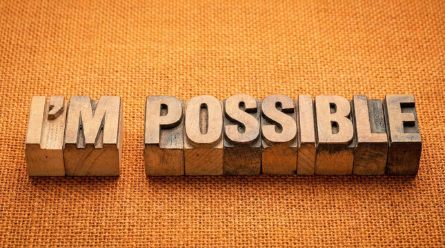 Wooden letter blocks spell out 'im possible' on an orange fabric background