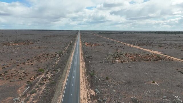 Aerial drone flight directly above a straight outback road cutting through dry, sparse wilderness toward the distant horizon in Australia