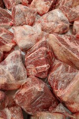 Close-up, overhead shot of various cuts of raw, uncooked pork meat, neatly wrapped in transparent plastic wrap, ready for sale or cooking, in a butcher shop display.
