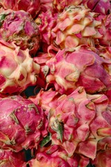Close-up photograph of vibrant, exotic dragon fruit display, showcasing the intricate textures and striking pink hues of the tropical produce against a blurred background, capturing a market