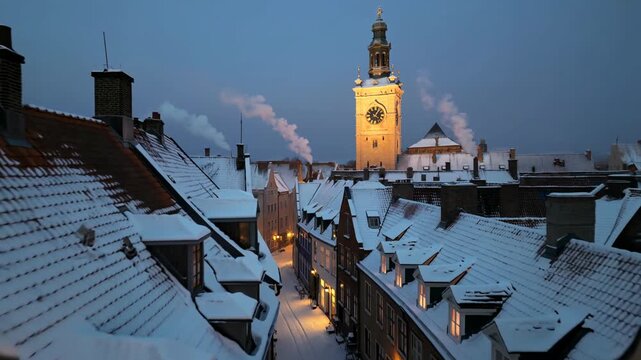 Snowy European town street at dusk with illuminated clock tower and smoking chimneys