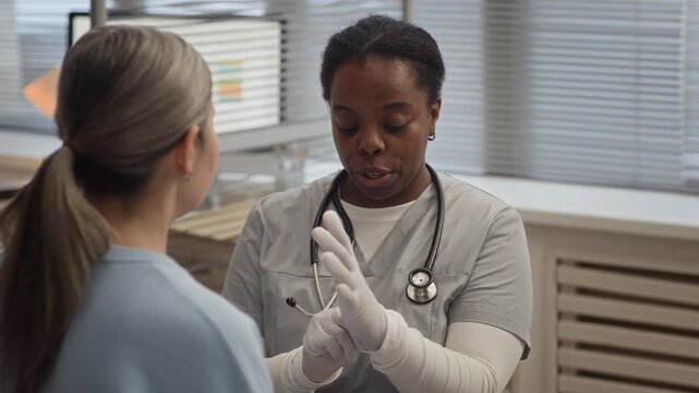 Black female doctor wearing scrubs and gloves preparing to examine neck lymph nodes during routine medical checkup in modern clinic