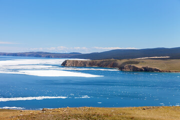 Baikal Lake at sunny May day. Spring landscape of ice drift on Small Sea near coast of Olkhon Island. First wildflowers are blooming on shore. Natural seasonal background. Spring travel and outdoors