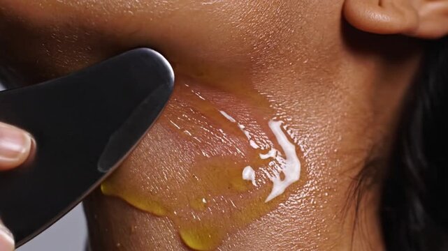 Slow motion close-up of a Gua Sha tool gliding over oiled skin on the neck and jawline, promoting facial massage and wellness.