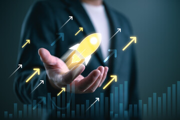 Businessman holding glowing rocket icon with upward arrows and growth chart. Concept of startup...