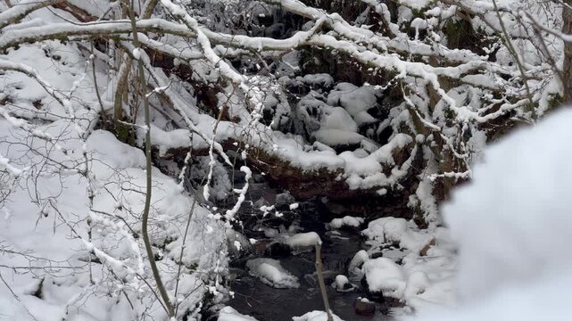 A hike to a snow-covered waterfall in Grantown-on-Spey, Cairngorms National Park. Dava Way. Winter snow-covered forest and a river flowing over rocks.