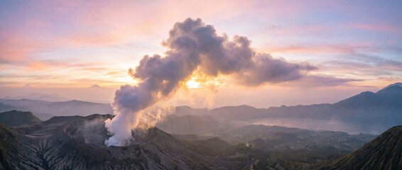 Mount Bromo volcano emitting smoke at sunrise with colorful sky and mountain range in Indonesia