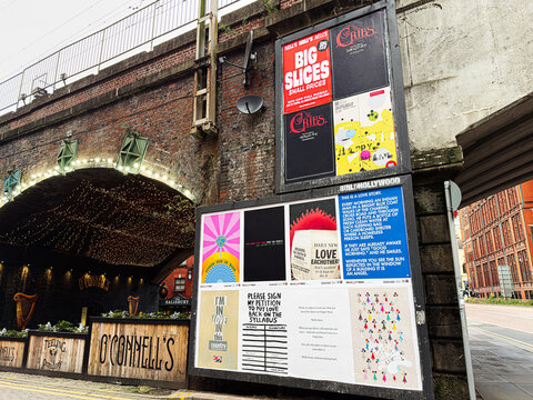 Manchester street scene with posters and lights under a brick underpass by O'Connell's Irish Bar pub display