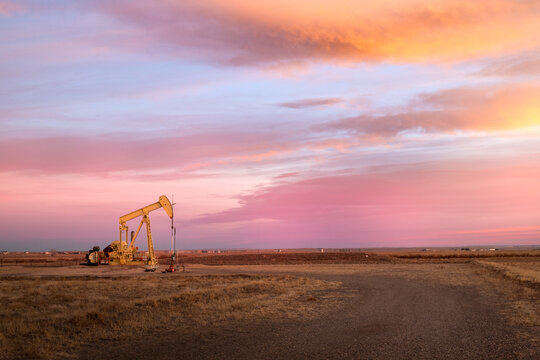 An oil pump jack on the middle of a field with a sunrise cloudy sky