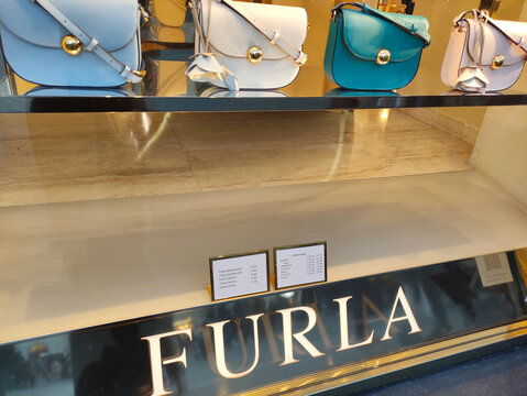 Rome, Italy - February 15, 2026: Display of Furla handbags in a retail window, featuring various colors and styles arranged on a sleek glass shelf