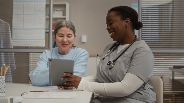 Female physician and patient reviewing medical test data on digital tablet while discussing diagnosis and care options in modern clinic
