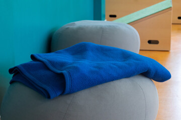 Blue fleece blanket neatly folded on a gray pouf in a modern interior with teal wall and wooden ramp structure in the background © Irina Flamingo