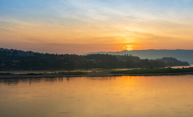 Colorful sunset sky above river and dark mountain landscape.