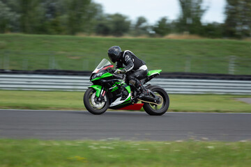 Professional racer in black gear riding a green and black sport bike at high speed on a racetrack circuit.