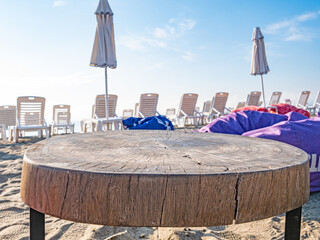 Wooden table on beach with chairs and umbrellas behind