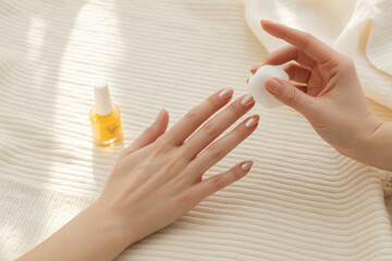 Female hands applying cuticle oil with brush on beige towel 
