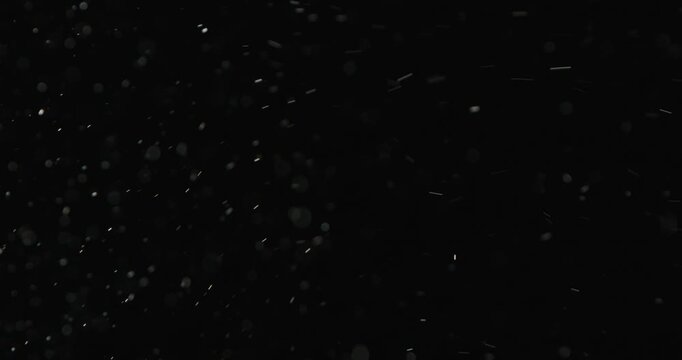 Tiny snow or dust randomly flying in the smoky air, empty space template for objects advertisement. Many dust particles cloud of white powder in low light on empty dark black contrast background.