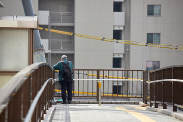 冬の昼の都市の歩道橋で街の工事現場を見るシニア男性の姿