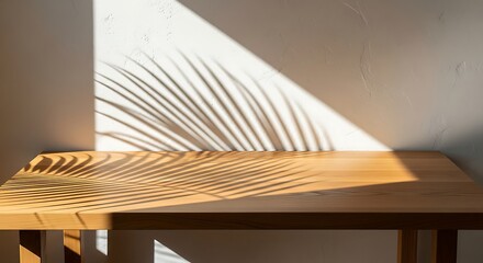 Sunlight casting palm leaf shadows on a wooden table and white wall