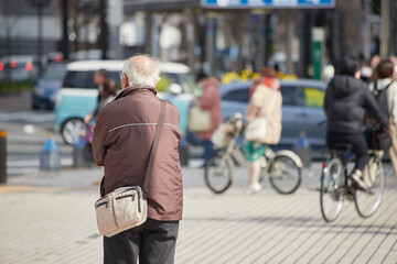冬の昼の都市の繁華街で信号待ちのシニア男性の姿