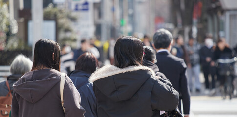 冬の昼の名古屋の繁華街の横断歩道を渡る若い女性と人々の姿
