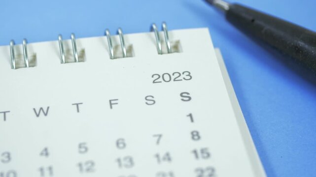 Macro view of 2023 desk calendar showing month and dates next to black pen on blue background
