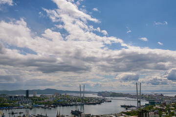 Obraz premium Panoramic view of Golden Bridge and Vladivostok harbor under blue sky.