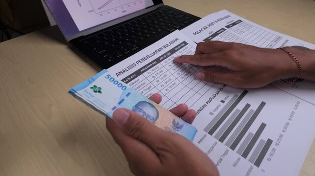 Hands Counting Indonesian Rupiah Near Laptop and Business Papers
