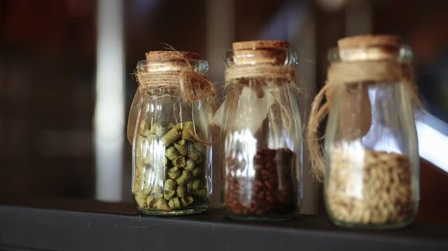 Brewery factory with grains and hops in jars amidst copper equipment for craft beer.