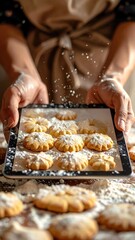 Hands holding a tablet displaying freshly baked golden brown cookies dusted with powdered sugar on a wooden table with scattered flour and cookies