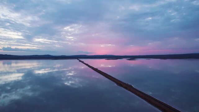 4K Aerial shot of beautiful road passing through salt water lake in Great Rann of Kutch. Road connects Khavda and Dholavira villages in Kutch, Gujarat. Scenic road after sunset, reflection of clouds i