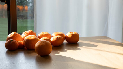 木目のテーブルに置かれたみかん 自然光が差し込む部屋 ミニマルな静物 / Fresh oranges on wooden table with dramatic natural light and shadows, minimalist still life
