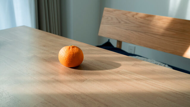 木目のテーブルに置かれたみかん 自然光が差し込む部屋 ミニマルな静物 / Fresh oranges on wooden table with dramatic natural light and shadows, minimalist still life