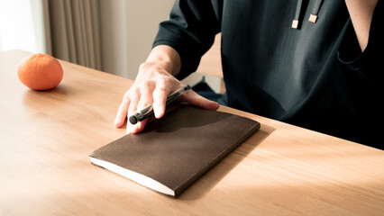 ノートに書き物をする男性の手元 思考の整理 ジャーナリング 丁寧な暮らし / Hands writing in notebook with pen and orange on table, journaling and planning concept