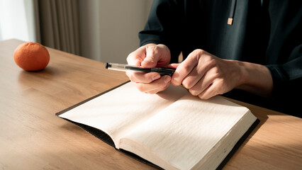 ノートに書き物をする男性の手元 思考の整理 ジャーナリング 丁寧な暮らし / Hands writing in notebook with pen and orange on table, journaling and planning concept