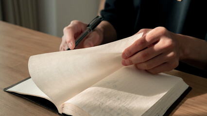 ノートに書き物をする男性の手元 思考の整理 ジャーナリング 丁寧な暮らし / Hands writing in notebook with pen and orange on table, journaling and planning concept