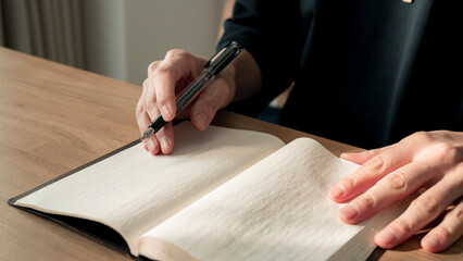 ノートに書き物をする男性の手元 思考の整理 ジャーナリング 丁寧な暮らし / Hands writing in notebook with pen and orange on table, journaling and planning concept