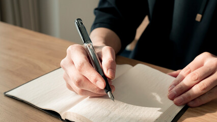 ノートに書き物をする男性の手元 思考の整理 ジャーナリング 丁寧な暮らし / Hands writing in notebook with pen and orange on table, journaling and planning concept