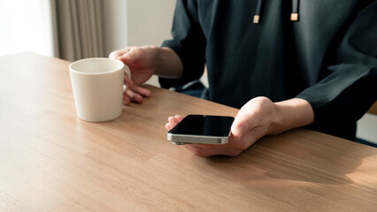 リラックスする男性の手元 スマートフォンとコーヒー ライフスタイル / Man using smartphone on wooden table, relaxed lifestyle