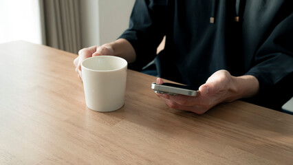 リラックスする男性の手元 スマートフォンとコーヒー ライフスタイル / Man using smartphone on wooden table, relaxed lifestyle