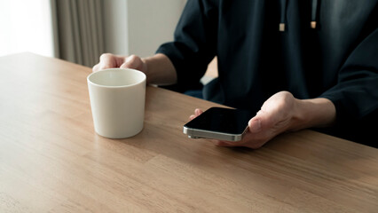 リラックスする男性の手元 スマートフォンとコーヒー ライフスタイル / Man using smartphone on wooden table, relaxed lifestyle
